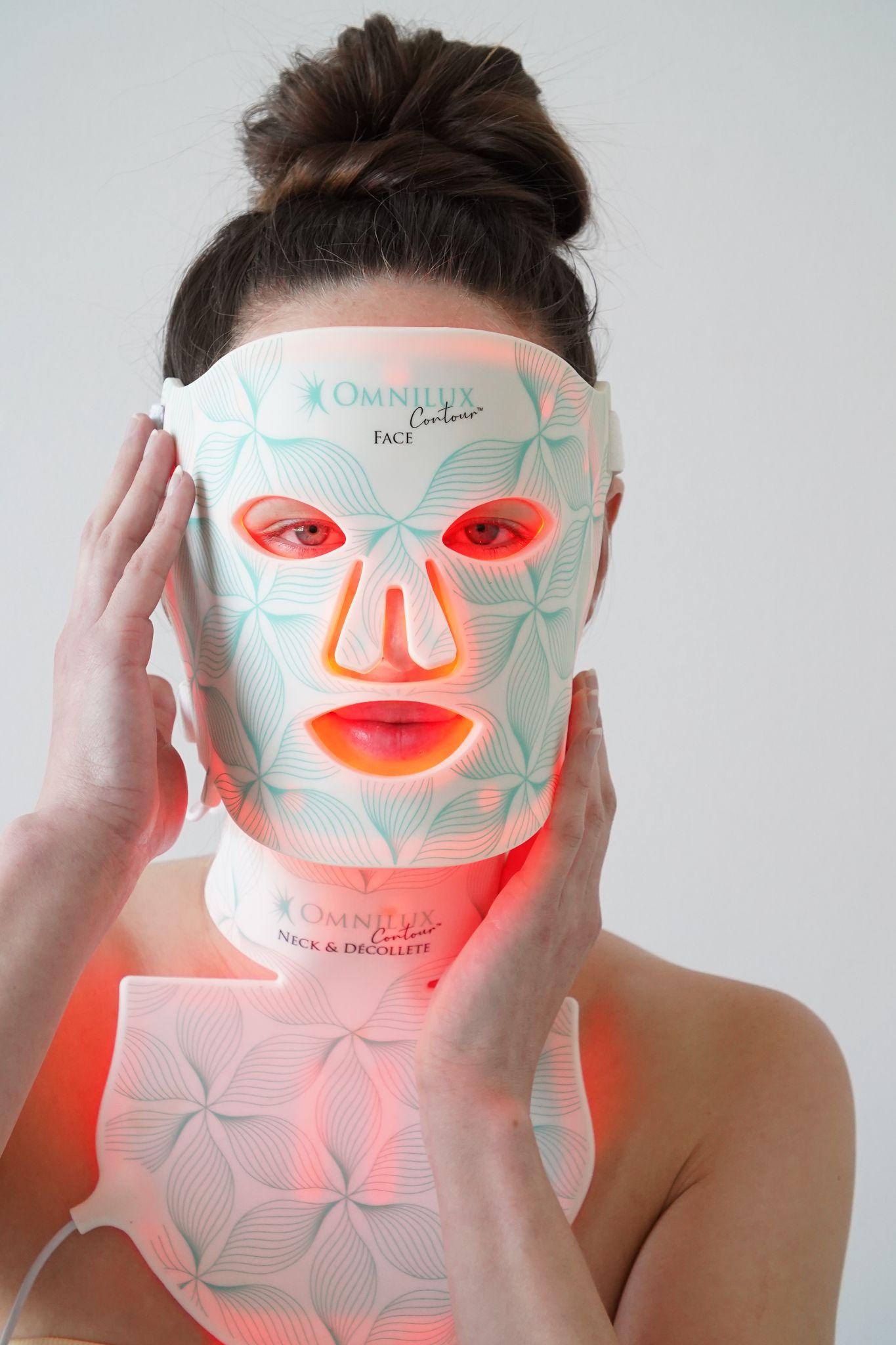 Woman wearing a glowing Omnilux Contour red light face mask and neck and d&eacute;collet&eacute; mask